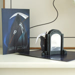 A dark-themed pop-up birthday card featuring the Grim Reaper holding a scythe. The cover says Happy Birthday, and inside, a tombstone with the text One day closer appears, adding a humorous, morbid touch to the card