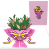 A 3D pop-up card featuring a bouquet of stylized pink and brown flowers with green leaves, wrapped in pink paper with a yellow and purple ribbon, next to a matching closed card with a bouquet illustration.