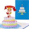 A pop-up card featuring a blonde woman in a red bikini emerging from a tiered birthday cake, holding a banner that says Happy Birthday. The card's cover shows a simple, decorated birthday cake with a candle on a blue background.