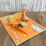 A pop-up card featuring a 3D kangaroo and another kangaroo lying down, set in a cartoon desert landscape with trees and rocks. The scene humorously illustrates an apology with the text, Sorry for destroying your Down Under.