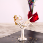 A pop-up card with a 3D figure of a woman lounging in a large martini glass, holding a cocktail stirrer. The card is set against a marble surface, with a colorful bouquet in the background, adding a playful, festive vibe.