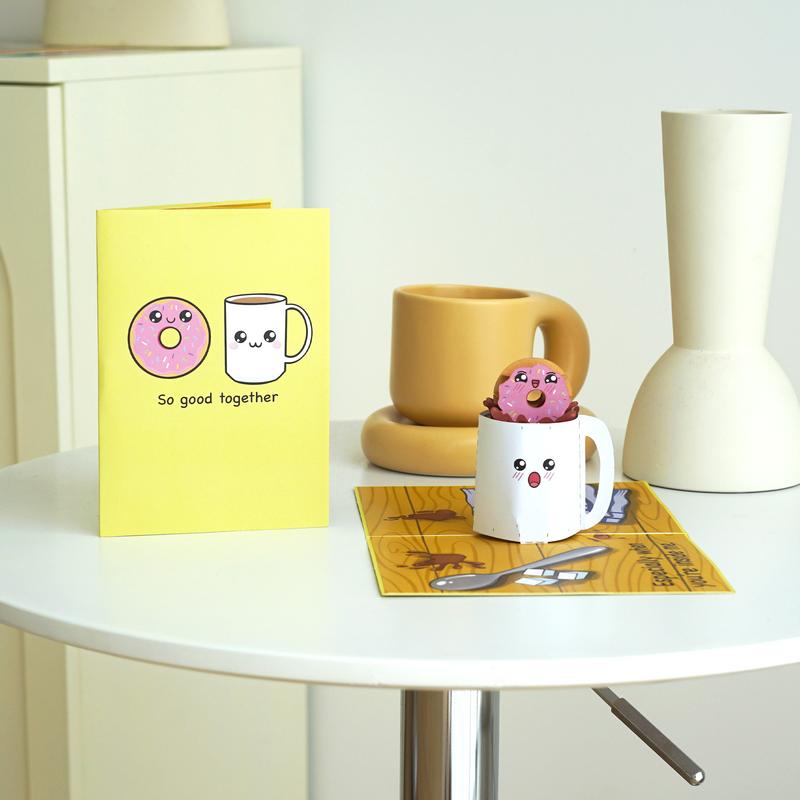 A cute pop-up card with a doughnut and coffee mug illustration on the cover, reading So good together. Inside, a 3D doughnut sits inside a smiling coffee mug, highlighting the fun and charming theme of the card.