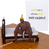 The image shows a humorous pop-up birthday card with a 3D figure of a muscular man sitting on a bed, wearing a party hat, with a CENSORED sign. The card's cover reads I wood like to wish you a Barry Happy Birthday!