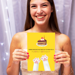 Smiling woman holding a yellow birthday card featuring a cake, cat paws, and the text "Purrfect Birthday."