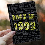 A person holds a greeting card with the text  BACK IN 1992 in bold yellow letters against a black background filled with retro phrases like Talk to the Hand and Da Bomb, with a blurred outdoor background